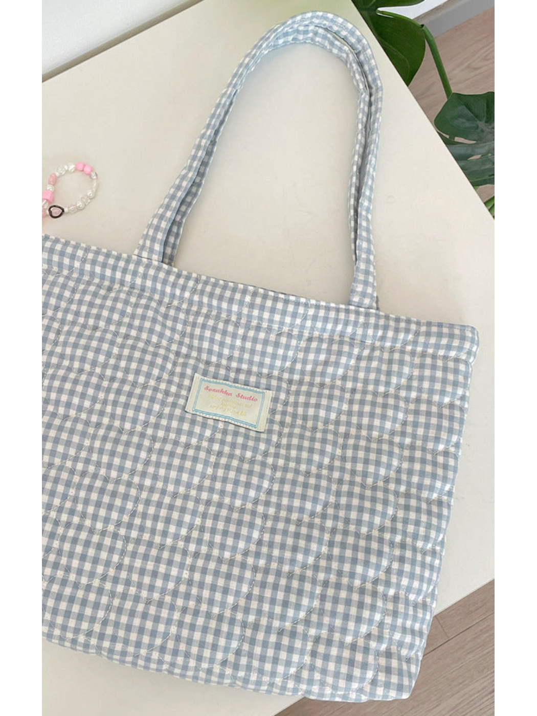 Limited detail of the Light Blue gingham tote, showing heart quilting, long handles and the front label