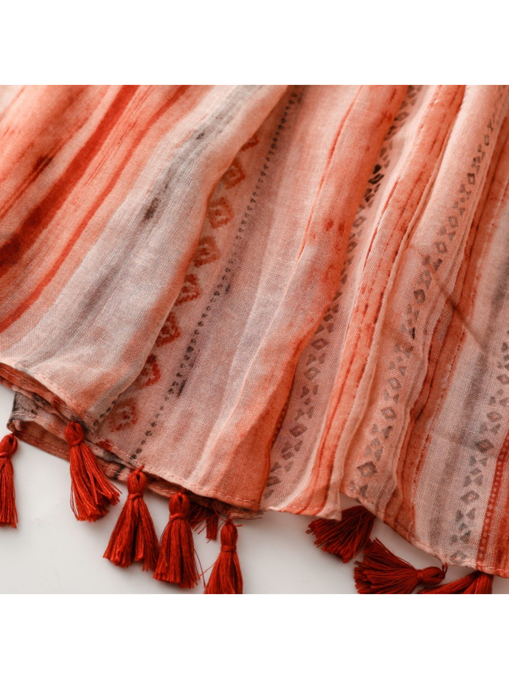 Close-up of orange red striped scarf ends with diamond motifs and red tassels