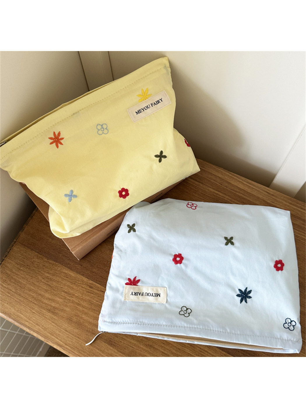 Yellow floral makeup bag standing behind a Blue bag laid flat