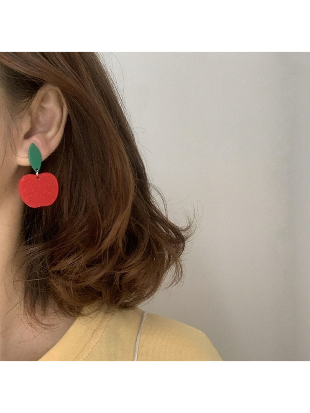Red apple drop earrings hanging from a jewelry stand with soft lighting