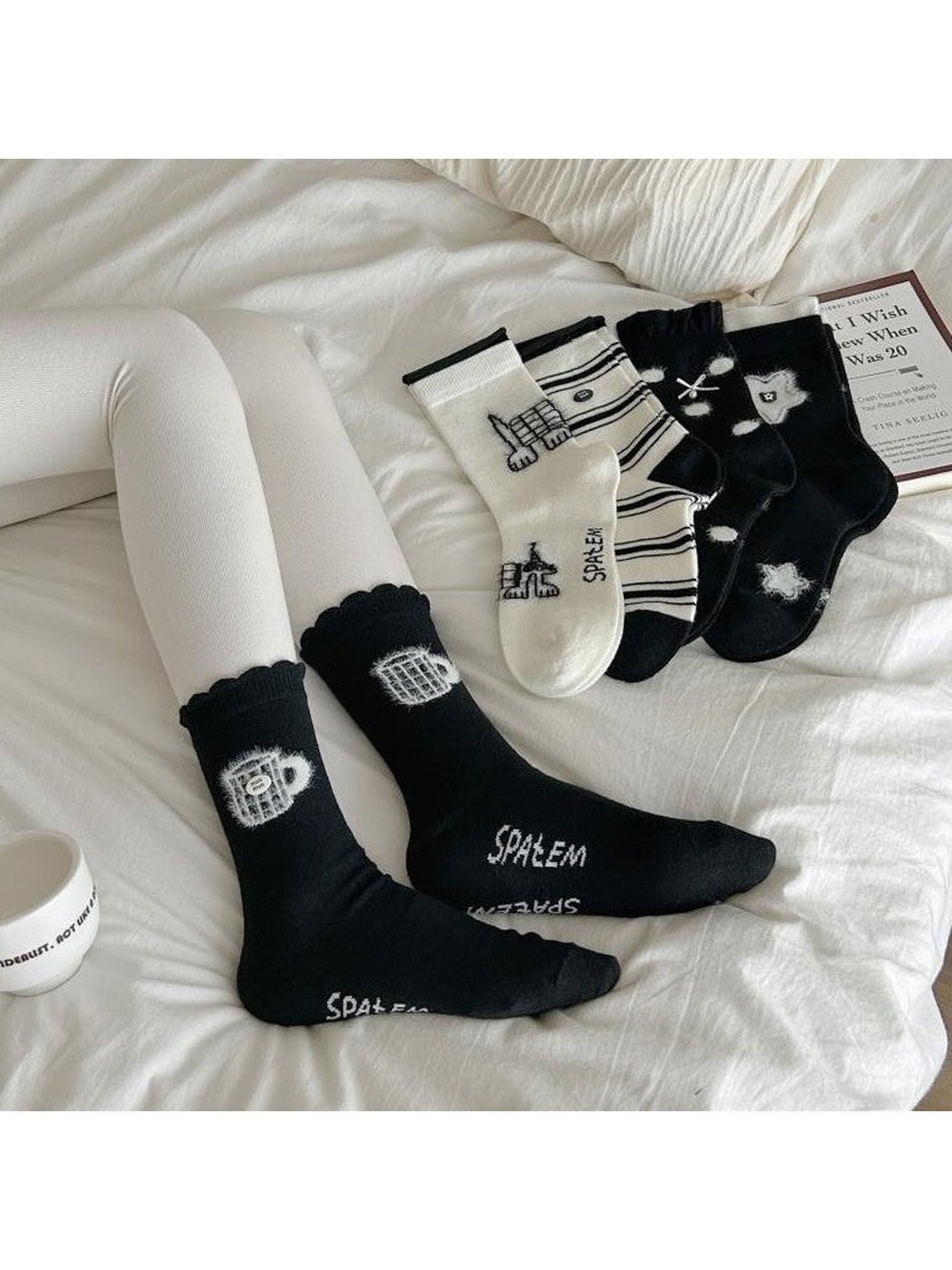 Black teacup socks worn on reclining legs, with other patterned socks arranged on the bedding.