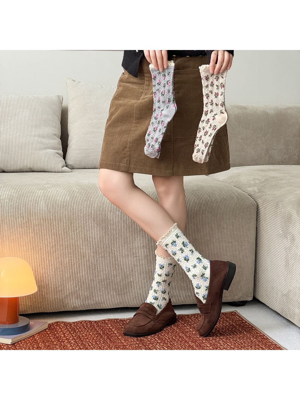 Ivory floral socks worn with brown loafers while gray and beige floral socks are held above.