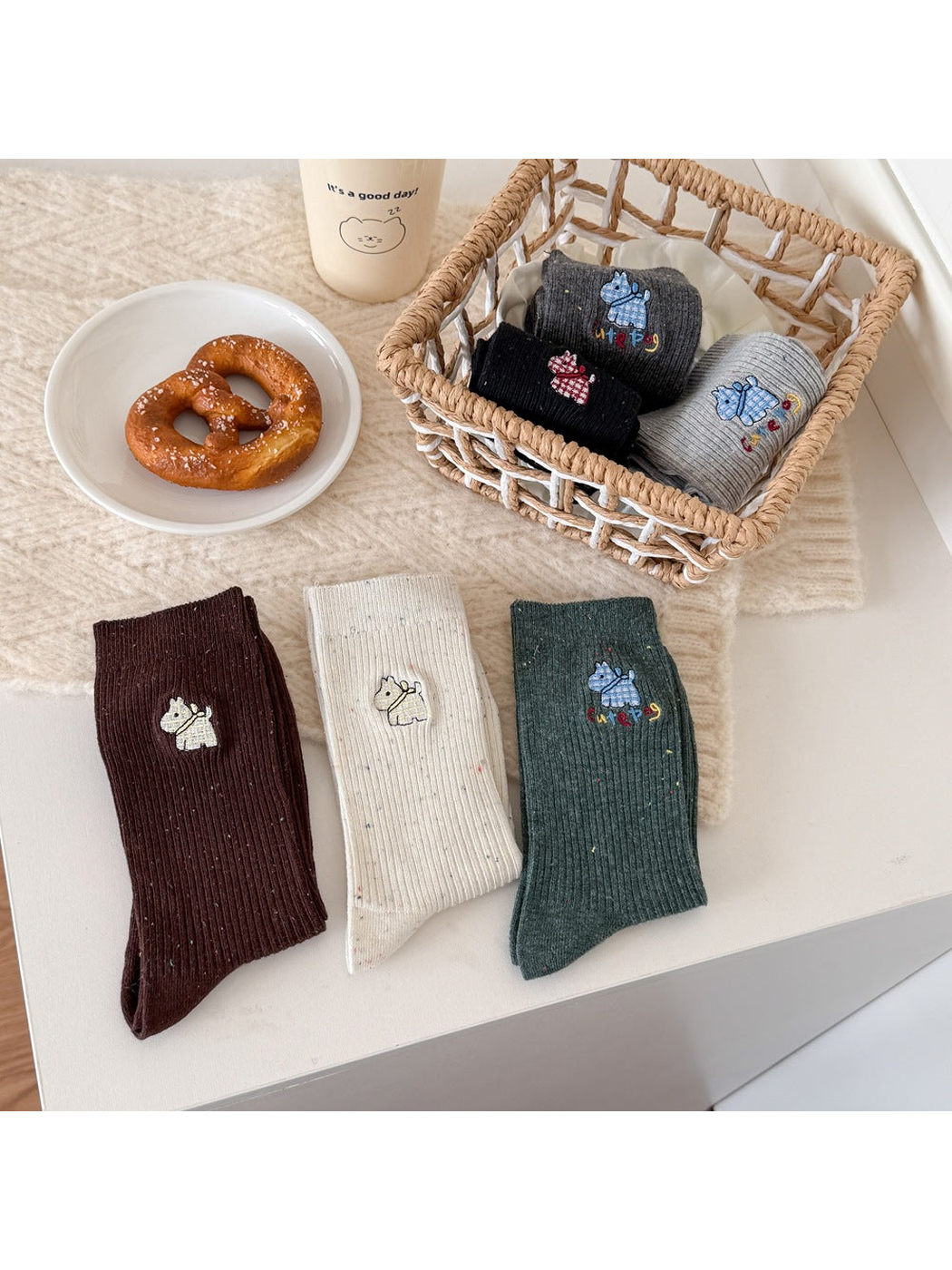 Brown, Ivory and Green dog-motif socks folded in front of a basket holding three other colors.