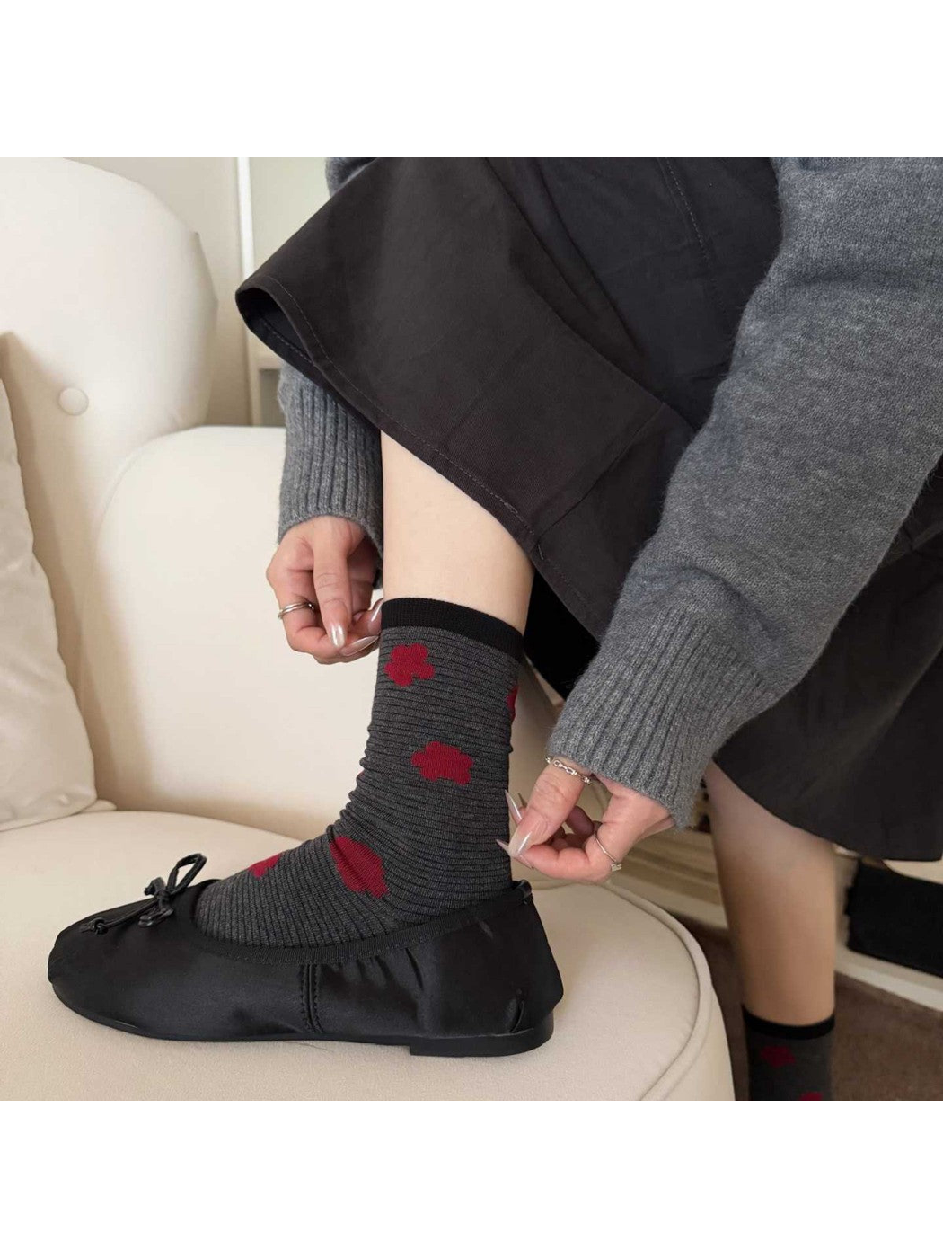 Gray socks with red flowers worn with black shoes as hands adjust one sock on a cream chair.