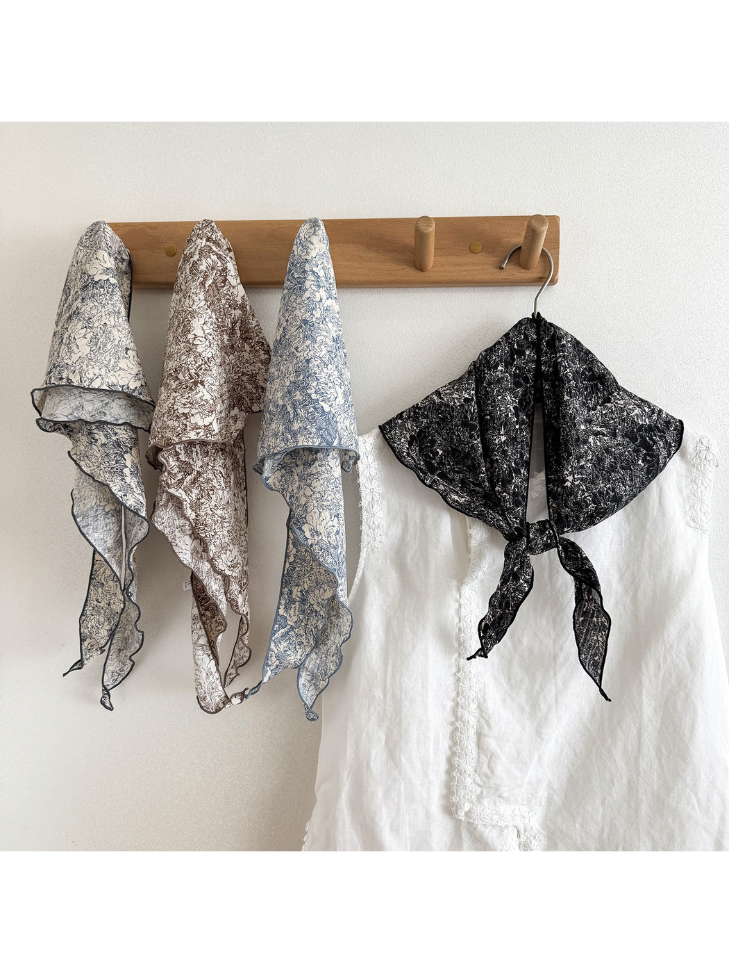 Ivory, Brown and Blue floral scarves hanging from wooden pegs beside a Black scarf tied over a white blouse.