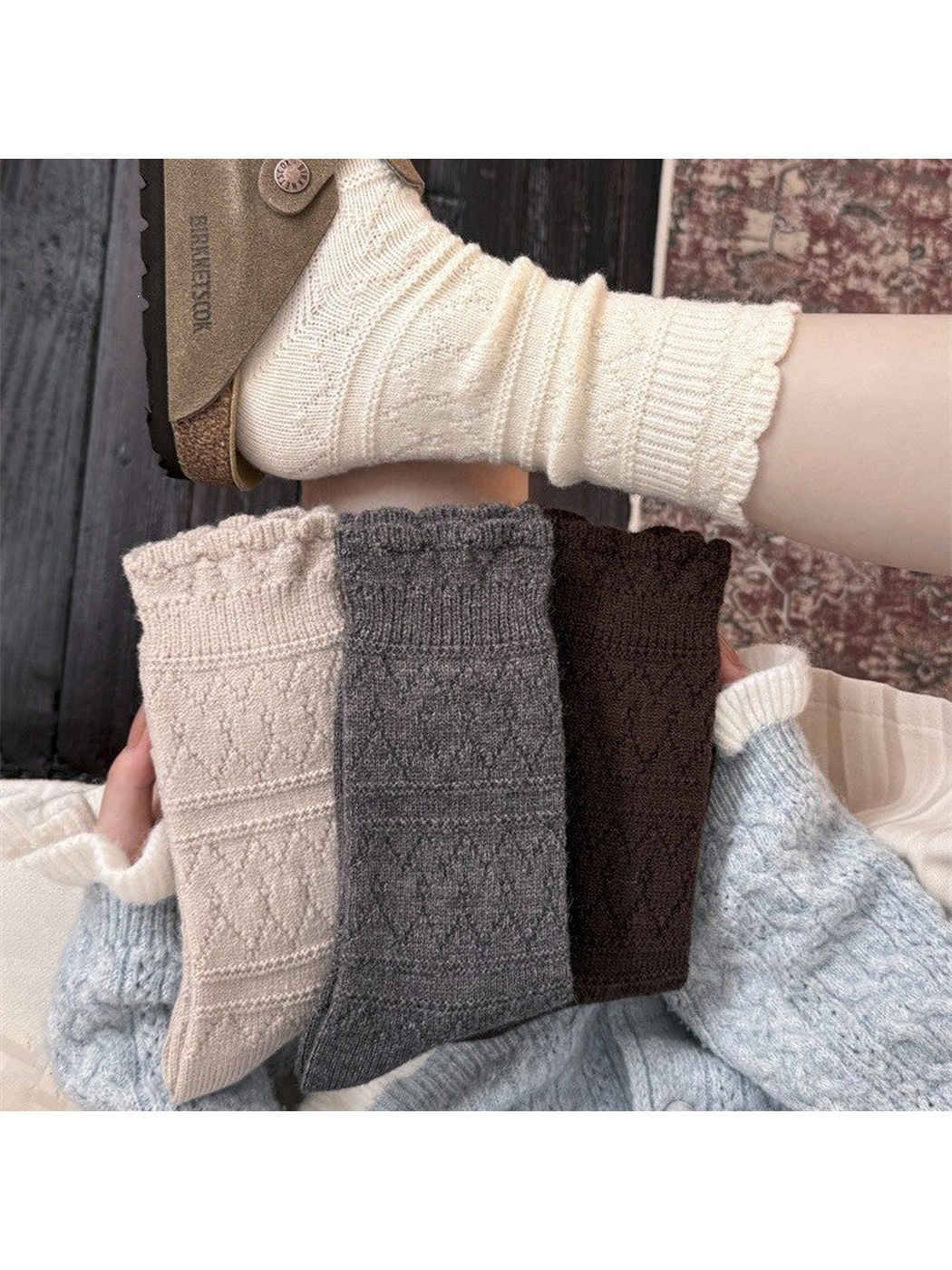Ivory socks worn with a sandal above folded beige, gray, and brown socks held in a hand.