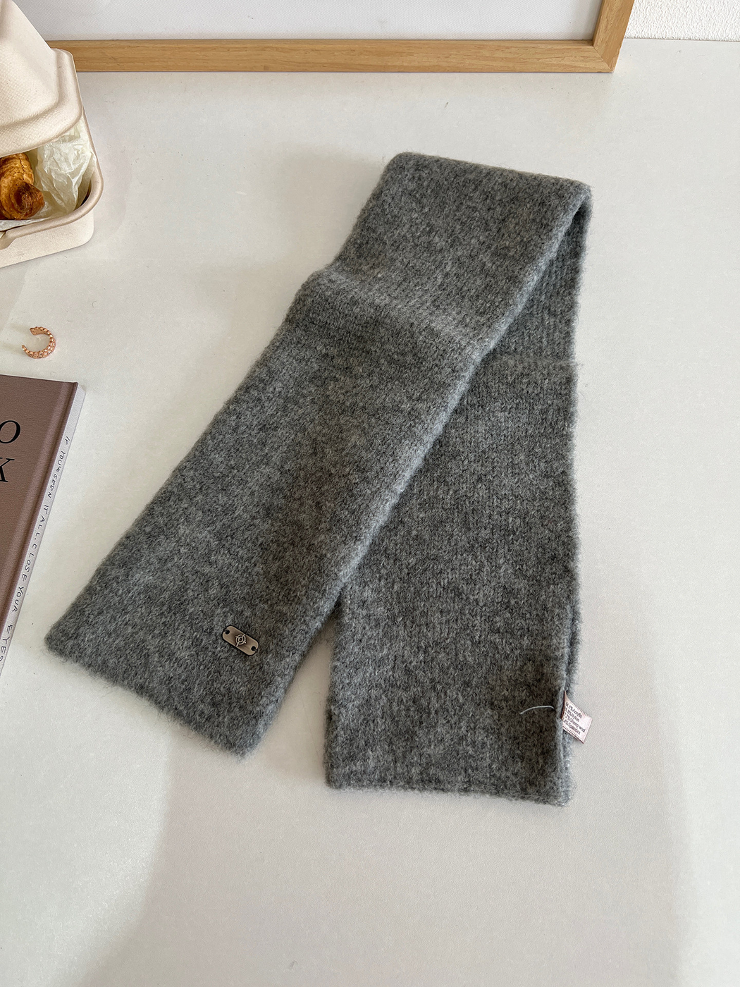 Dark gray narrow scarf laid out to show its full length, straight finished ends and metal-tone plaque