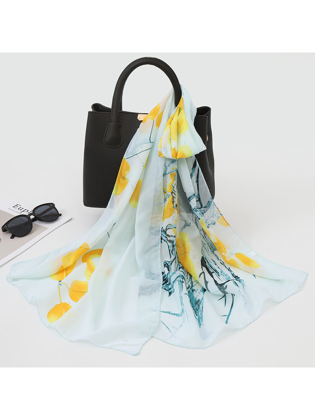 Mint green scarf with yellow botanical print draped over a black handbag