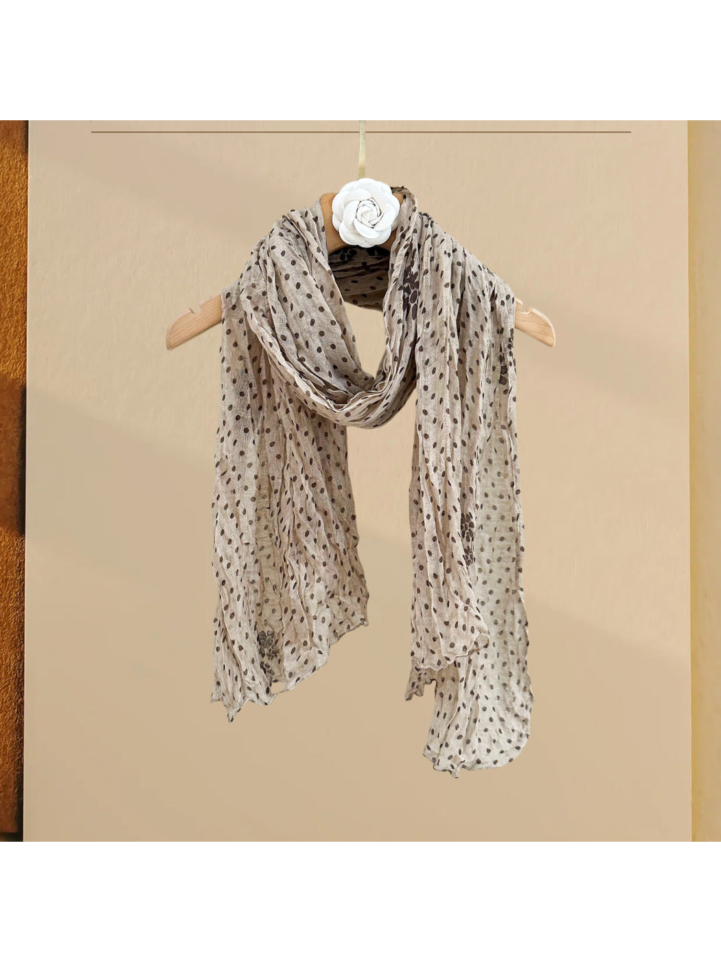 Beige polka-dot scarf with floral accents, draped on a hanger