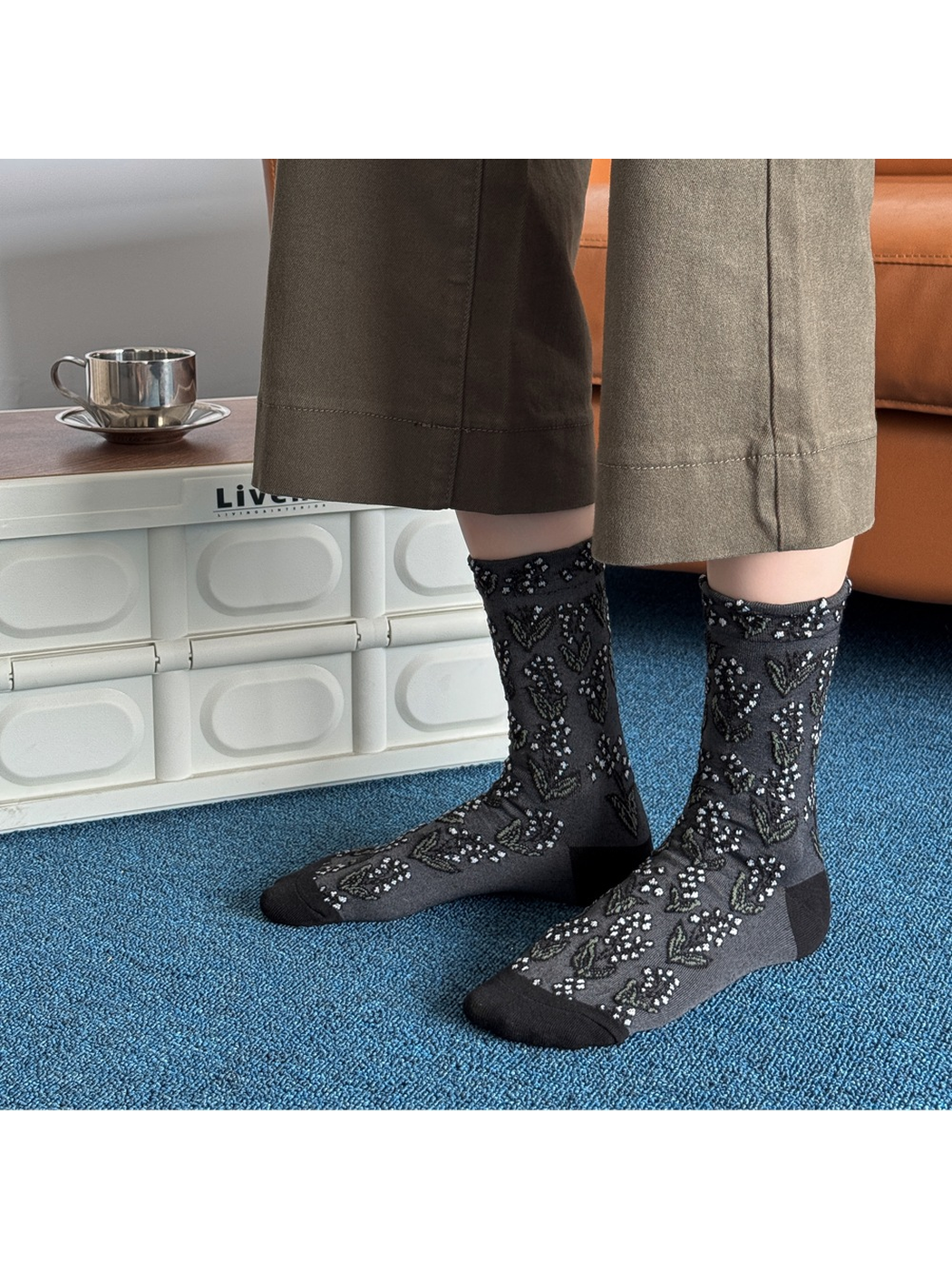 Black floral crew socks worn without shoes against a blue carpet
