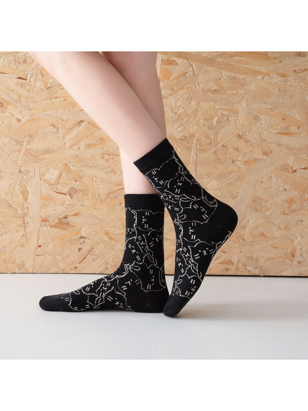 Black cat-pattern crew socks worn in a crossed-foot side view