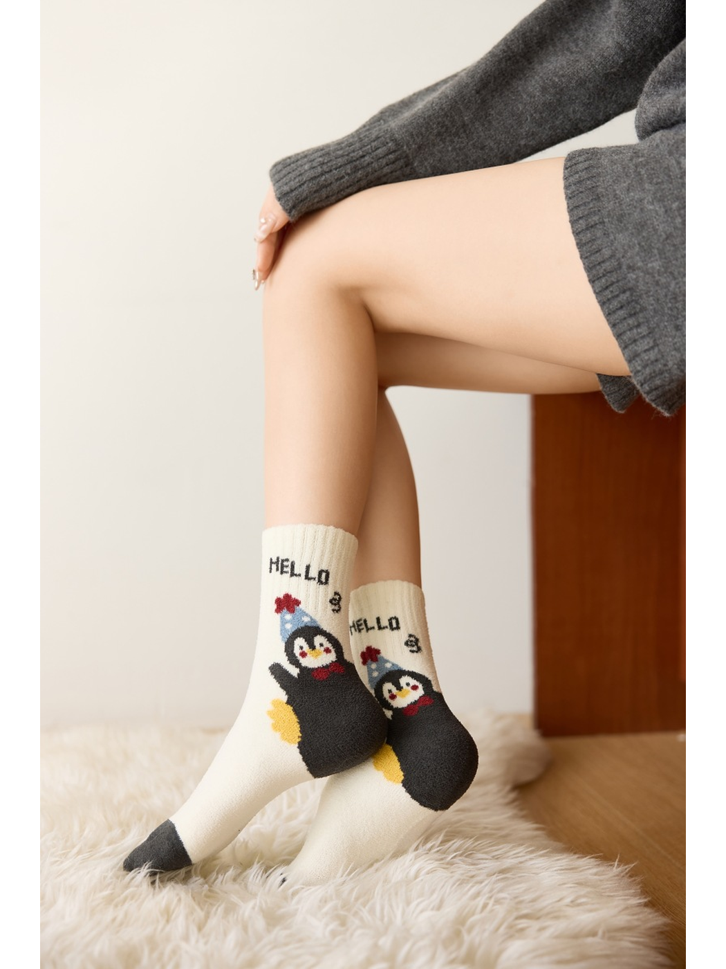 Ivory crew socks with large waving penguin graphics shown in a seated pose