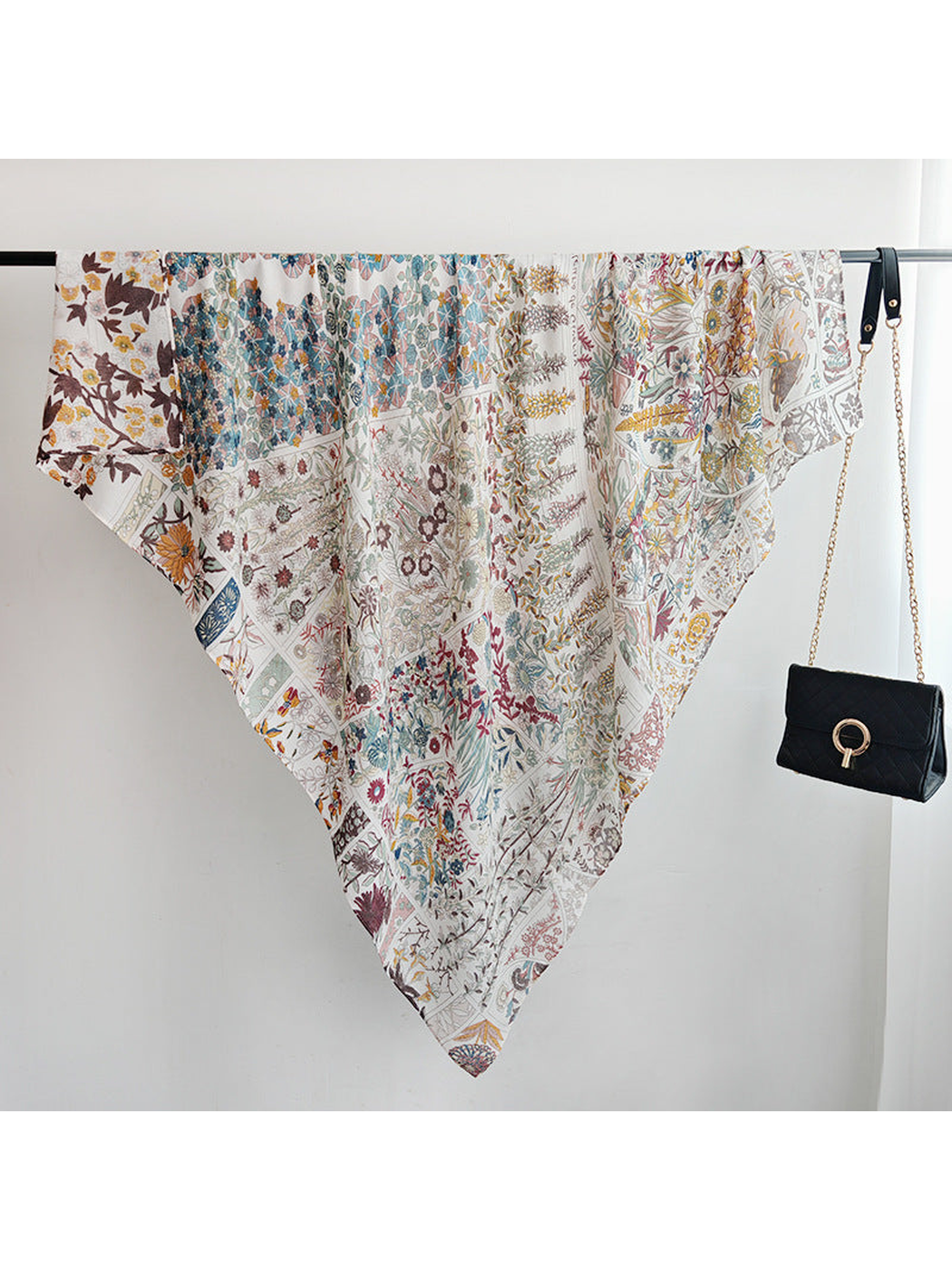 Botanical-print square scarf draped over a clothing rail beside a black handbag