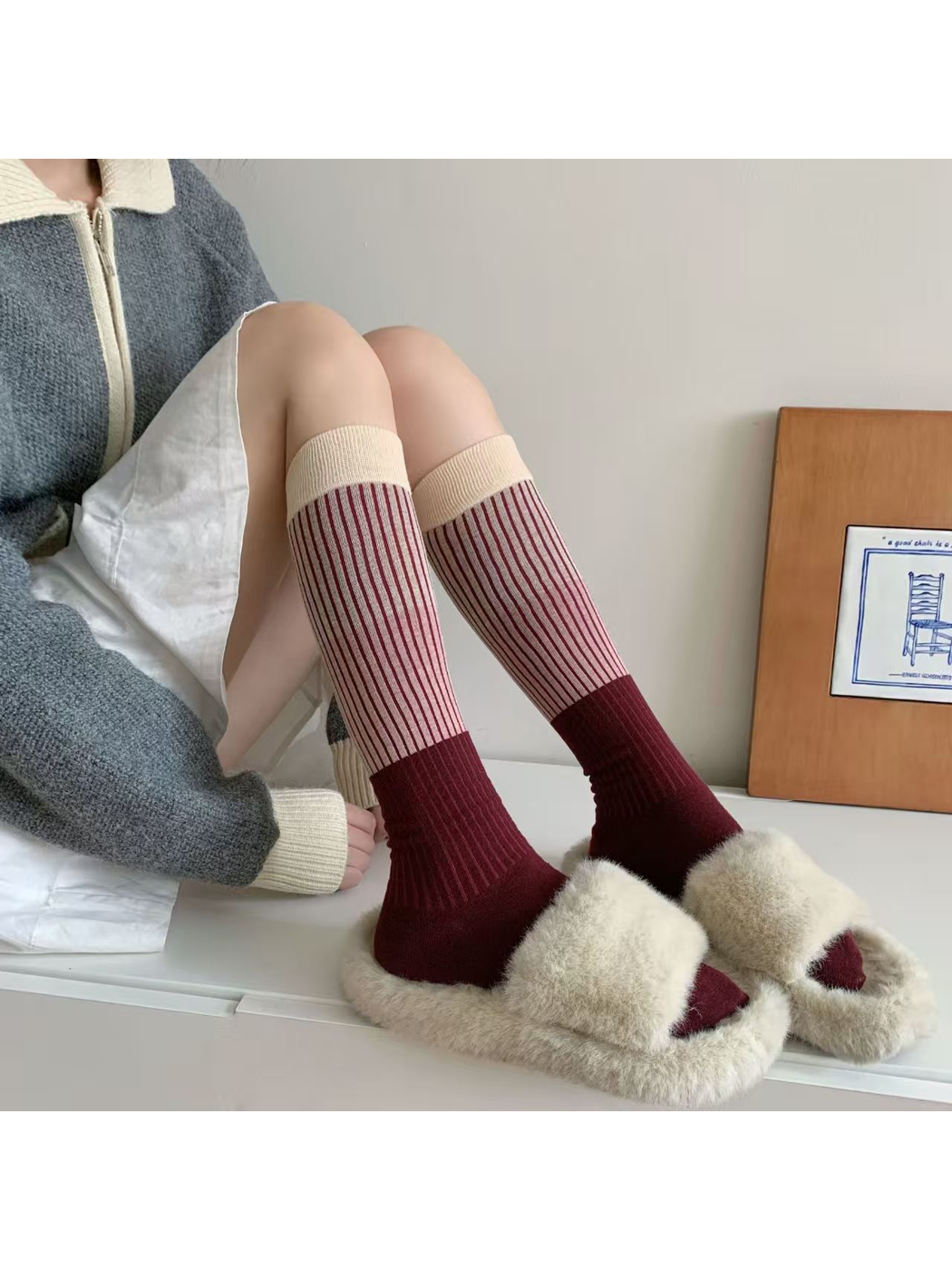 Burgundy knee-high striped socks styled with fuzzy cream slides