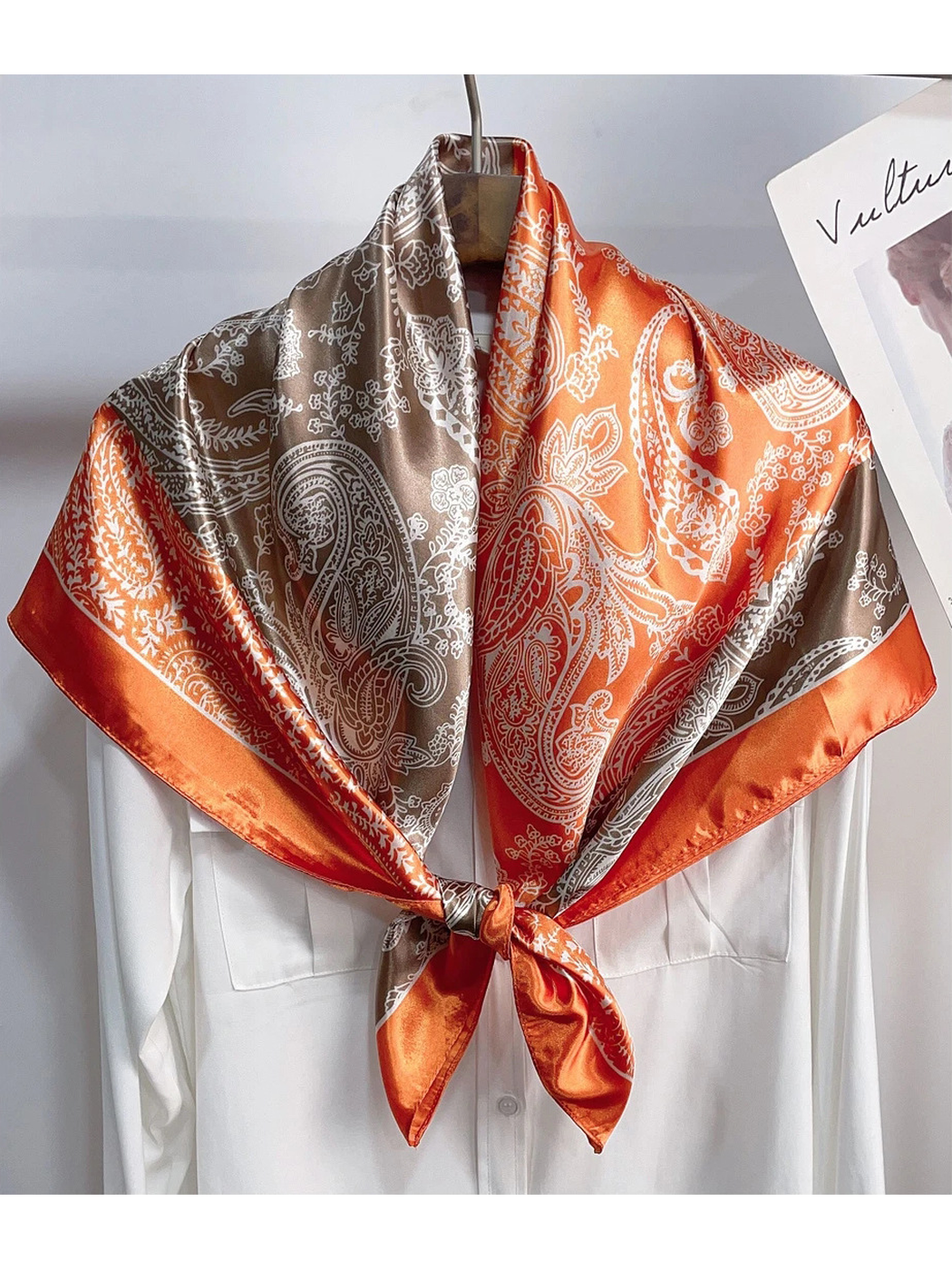 Orange and brown paisley scarf tied over a white shirt on a hanger