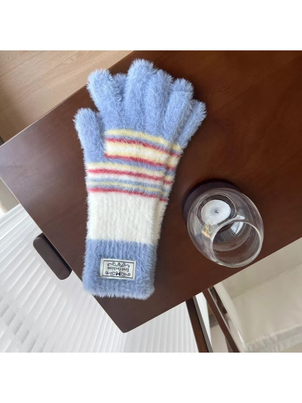 Light Blue fuzzy gloves with white panels and multicolor stripes, tabletop view