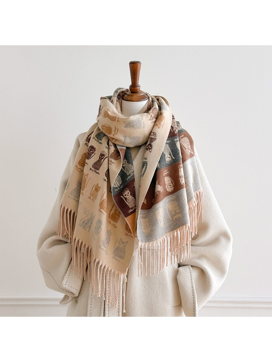 Beige cat-pattern scarf looped around a mannequin's neck, with long ends displaying both patterned sides over a white coat.
