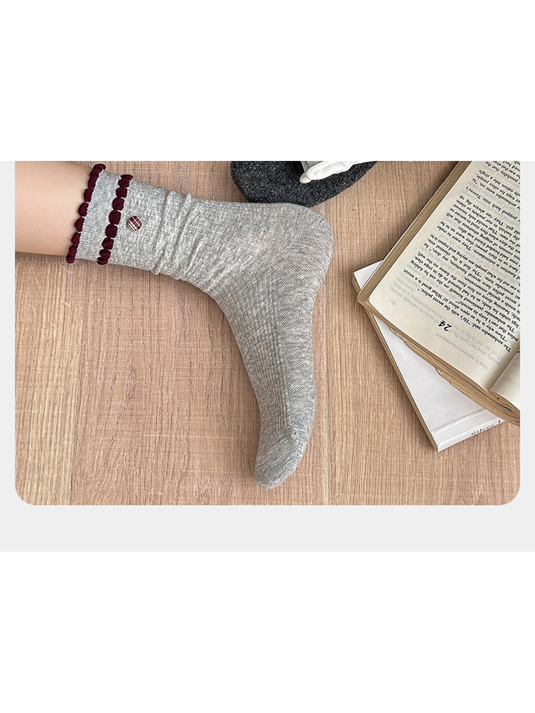 Heather gray sock with burgundy ruffled trim worn beside an open book, showing the heel and toe profile.