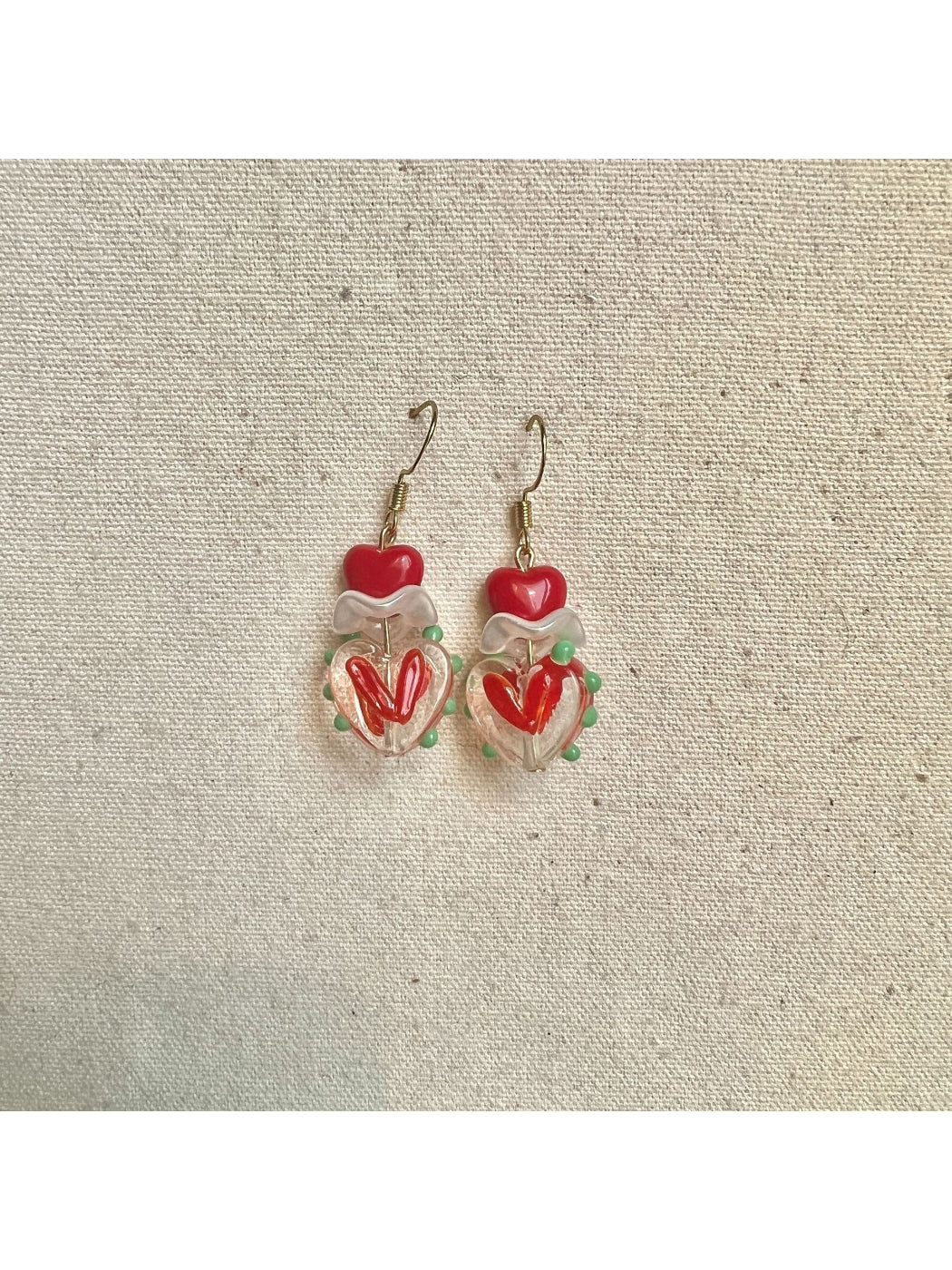 Pair of Earwish Playful Apple Heart Earrings placed on a wooden surface