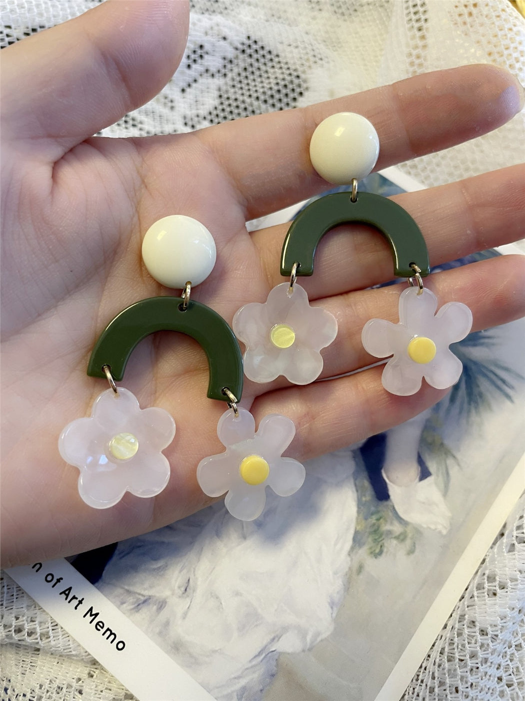 Green arch daisy earrings hanging from a jewelry stand with natural lighting