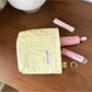 Cosbai pastel check zip pouch placed on white surface with soft lighting
