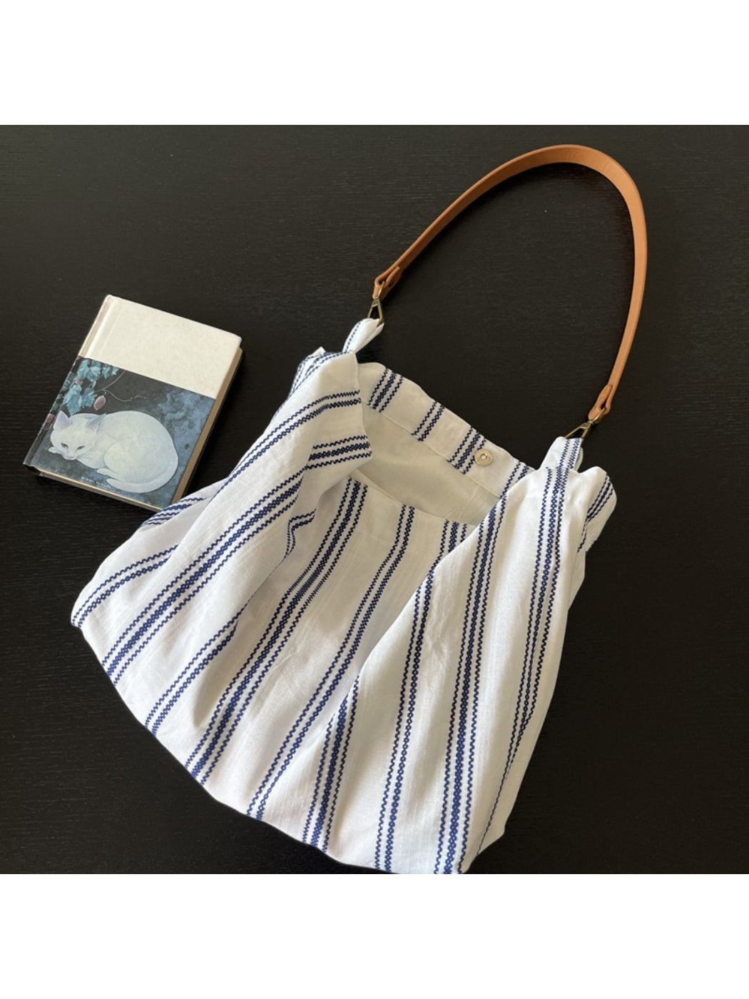 Cosbai blue stripe slouch shoulder bag hanging on a hook against a white wall