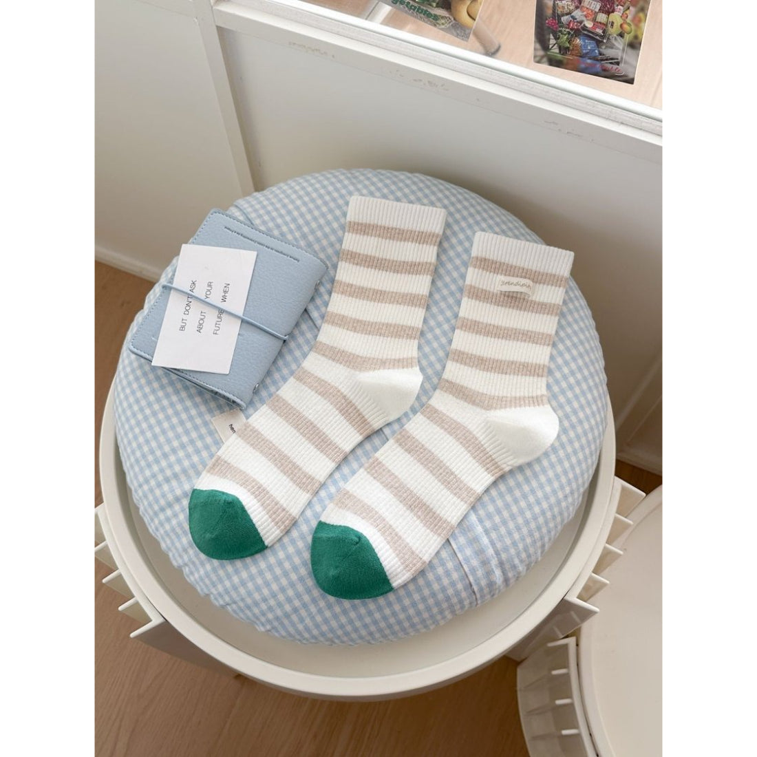 Rufia crew socks in beige with white stripes shown on wooden floor