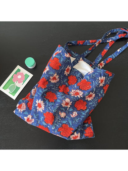 Blue floral shoulder tote bag resting on wooden surface with sunlight