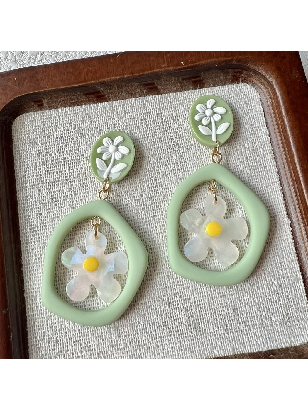 Close-up of green daisy hoop earrings with detailed petals and gold hoops