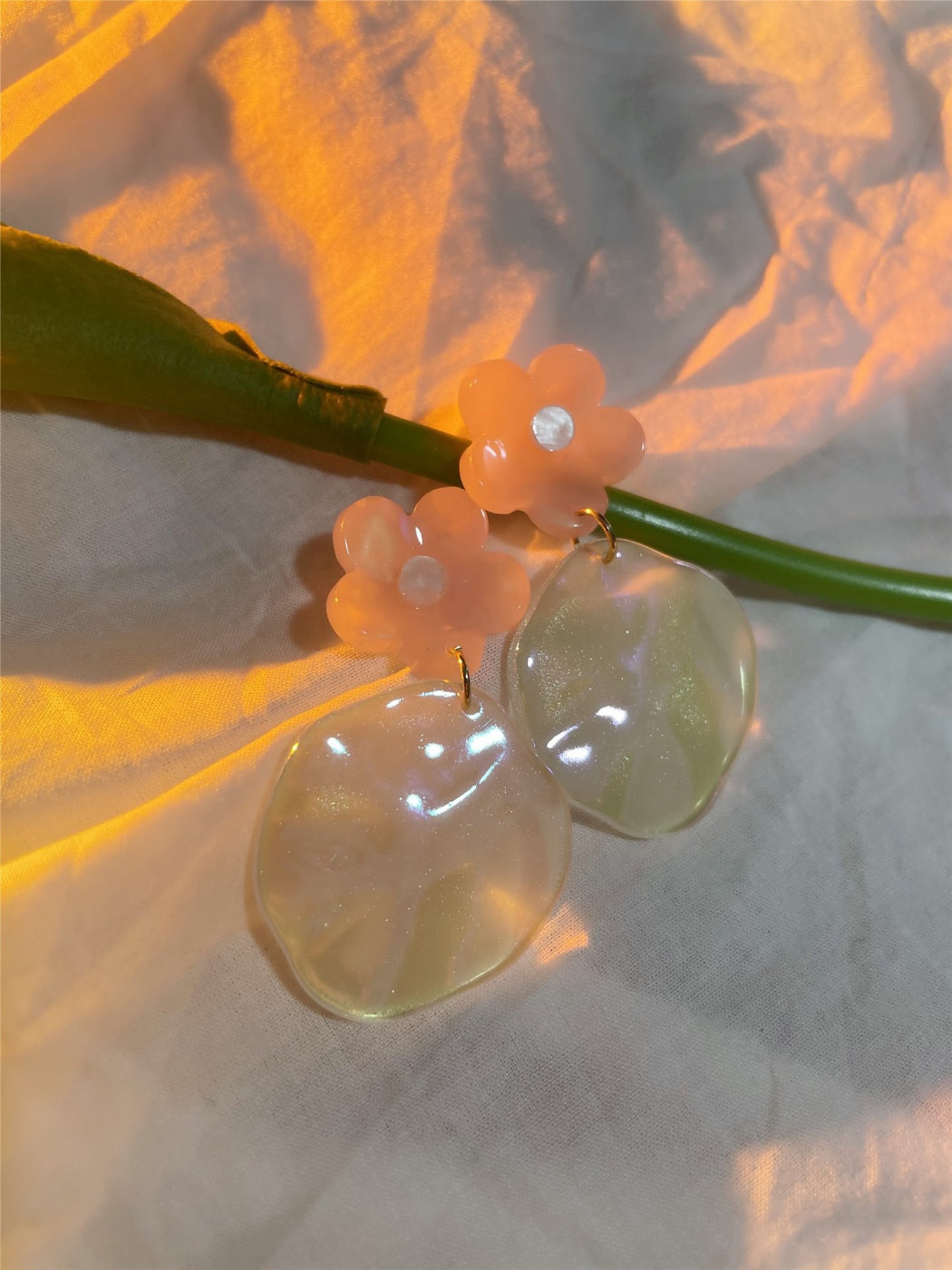 Glossy floral drop earrings displayed on a jewelry stand with soft lighting