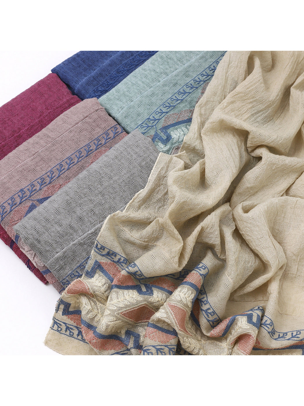 Close-up of folded scarves beside a draped scarf with a geometric and leafy border