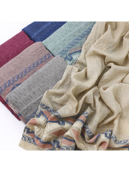 Close-up of folded scarves beside a draped scarf with a geometric and leafy border