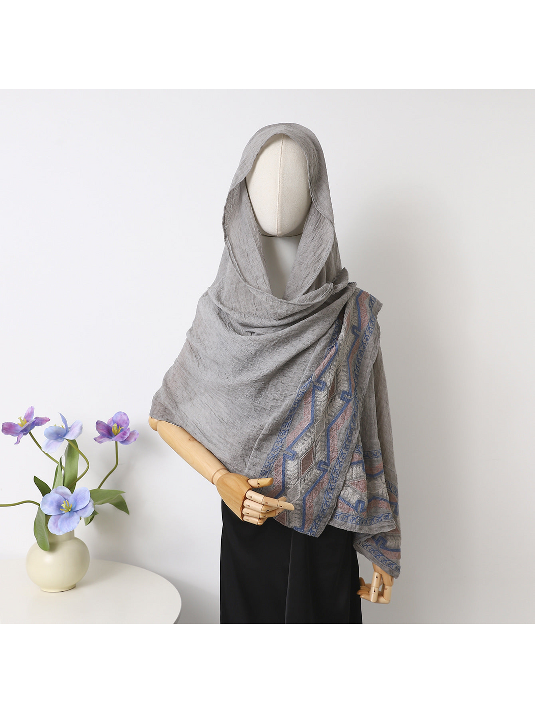 Gray scarf draped over a mannequin's head and shoulders with geometric border visible