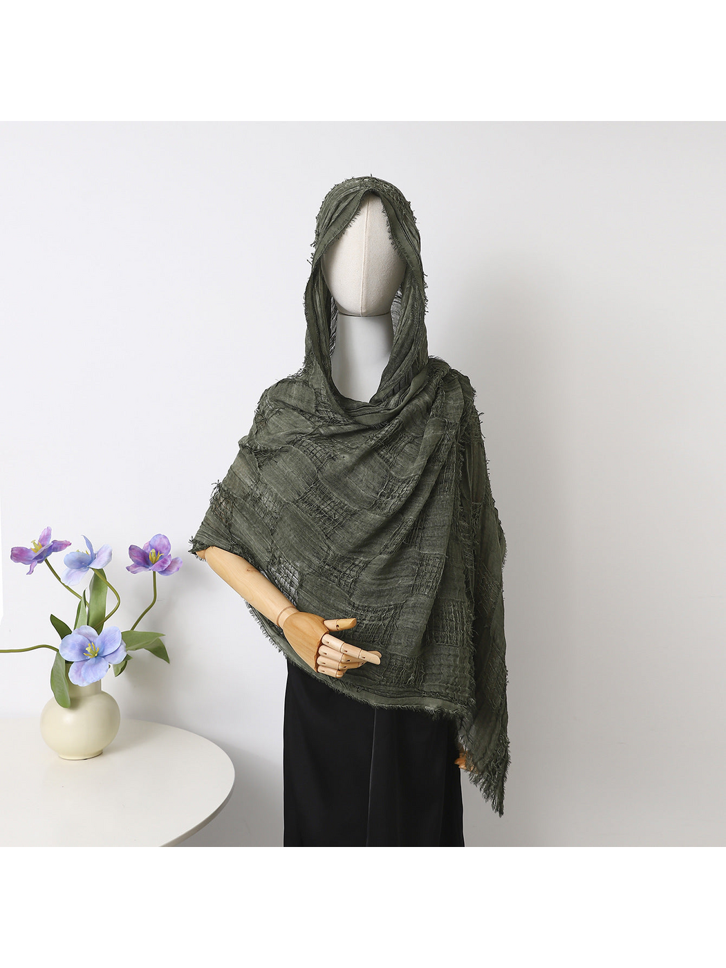 Green scarf draped over a mannequin’s head and shoulders, showing textured bands and fringed edges