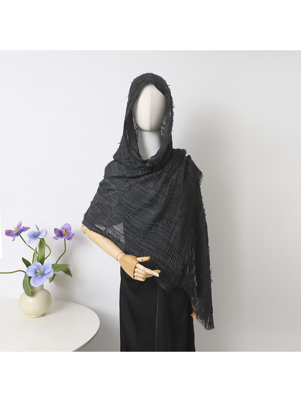 Black scarf draped over a mannequin’s head and shoulders, showing openwork bands and fringed edges