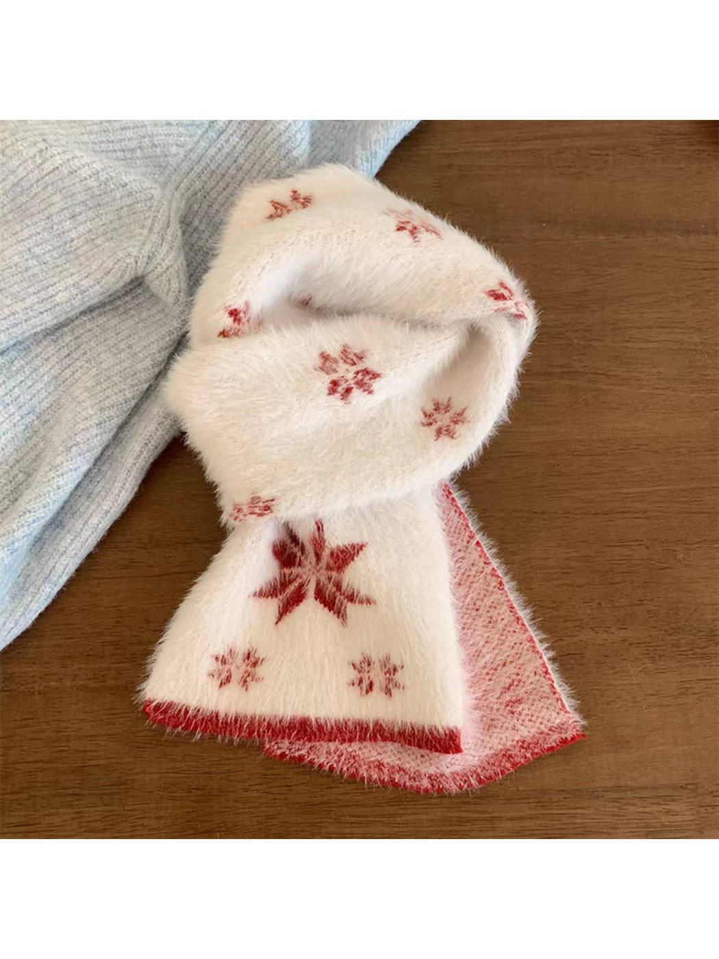 Red scarf with snowflake motifs and contrasting border, looped on a wooden table