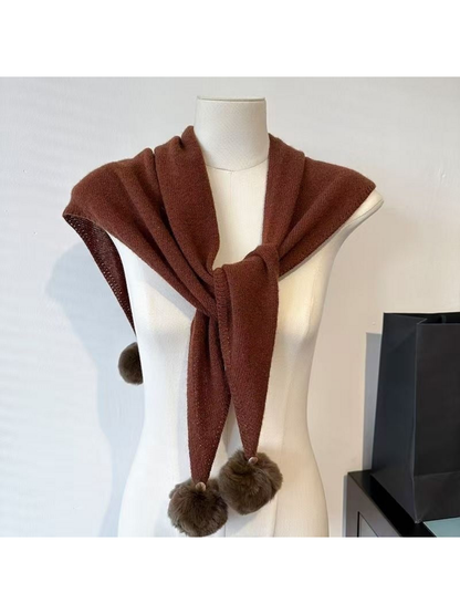 Brown knit scarf loosely tied across a mannequin's shoulders, with pom-pom ends