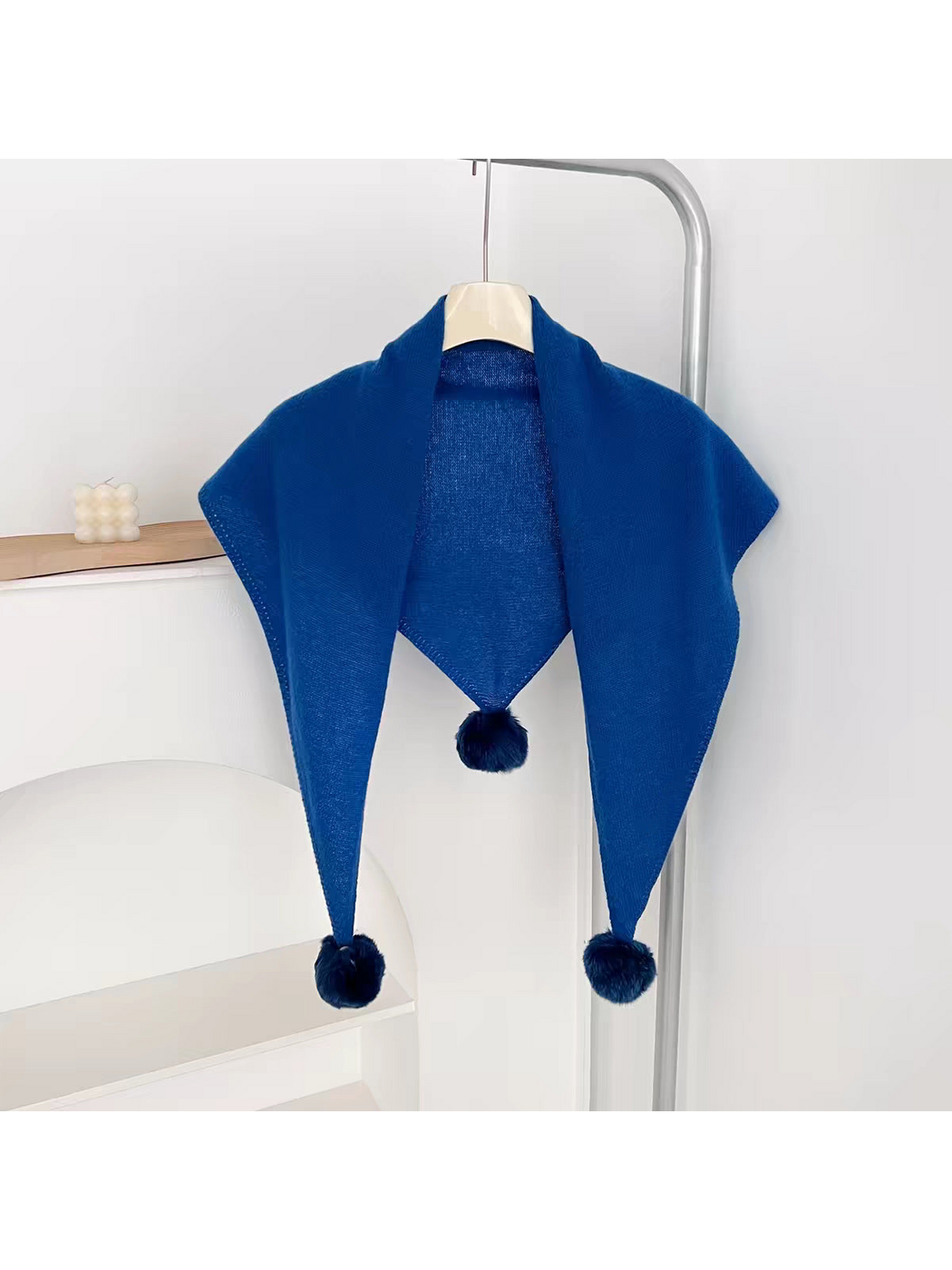 Blue knit triangle scarf hanging open with three pom-poms