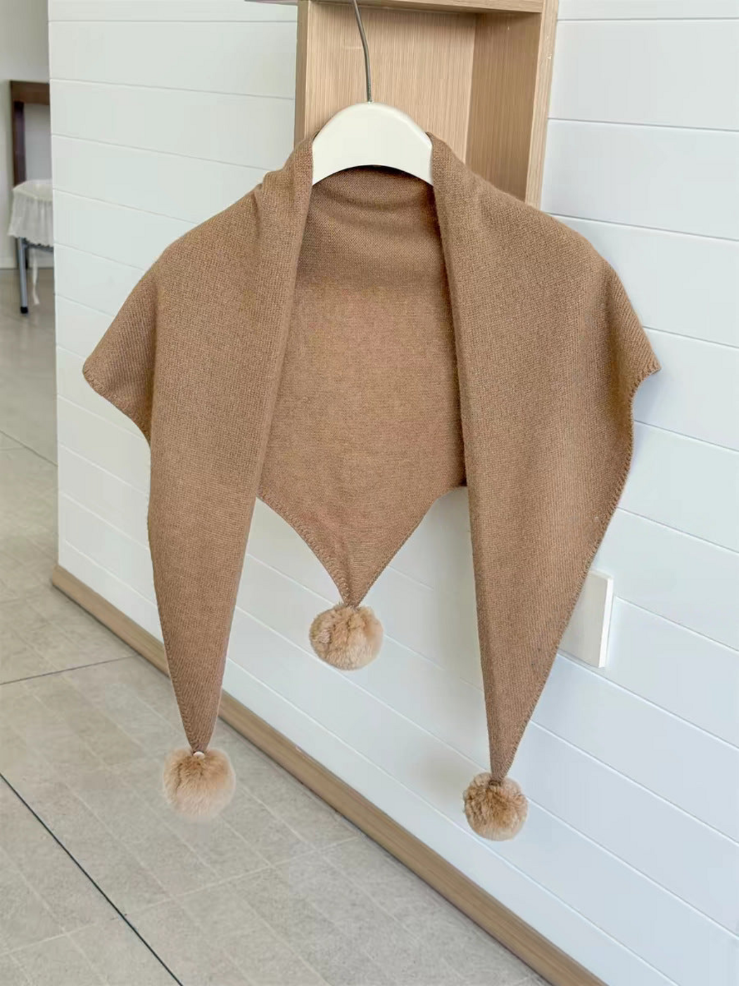 Camel knit triangle scarf hanging open with three pom-poms
