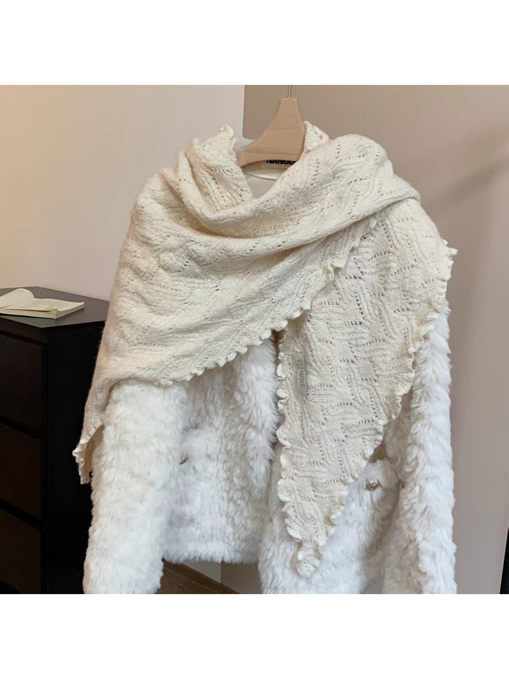 Ivory triangle scarf with openwork knit and scalloped edges draped over a white coat