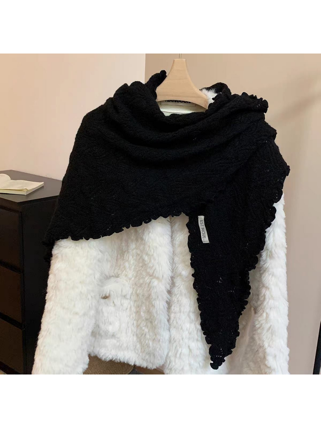Black triangle scarf with scalloped edges draped over a white coat