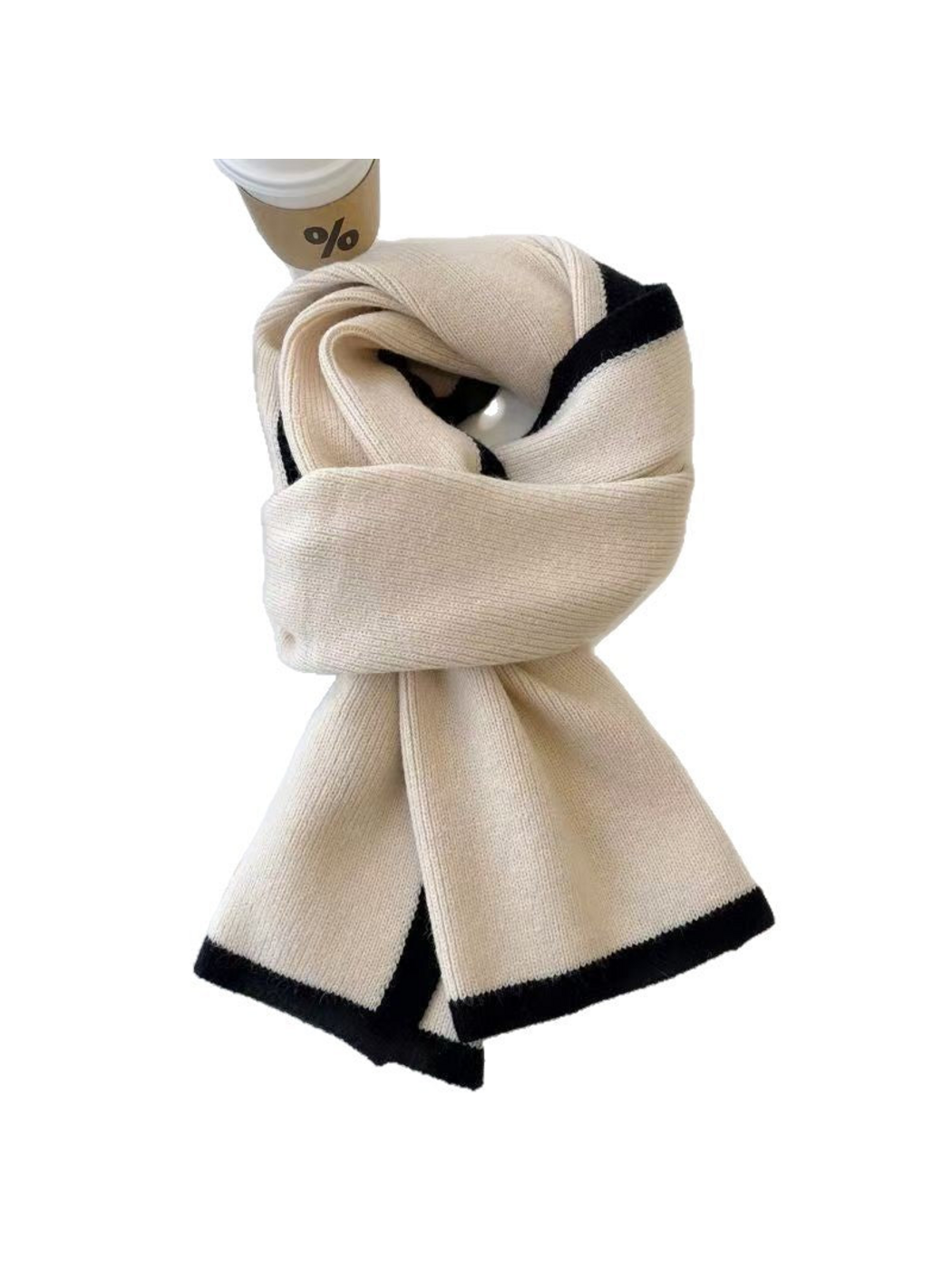 Cream knit scarf with black border trim, looped on a white background beside a coffee cup