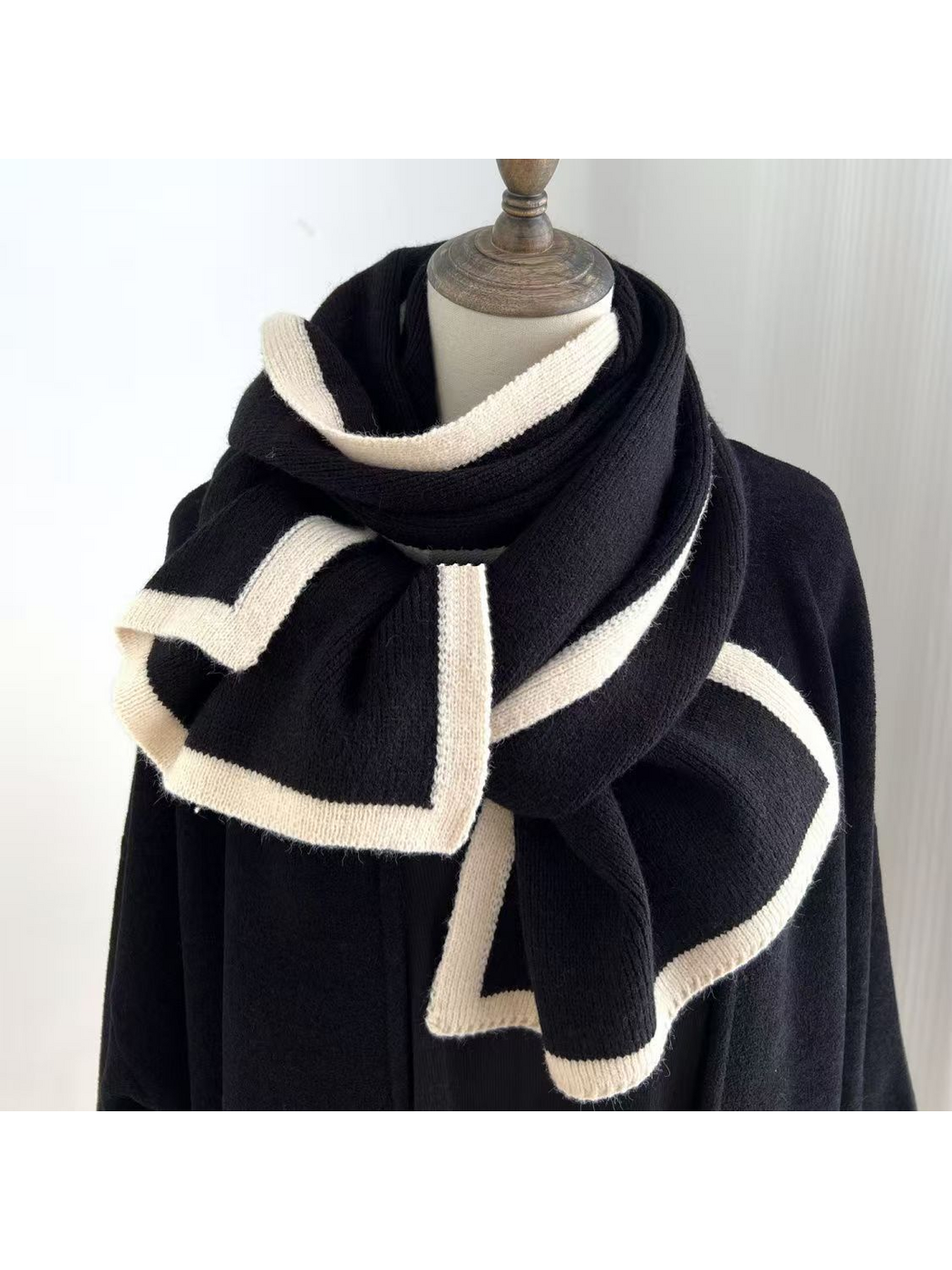 Black knit scarf with cream border stripes draped around a mannequin