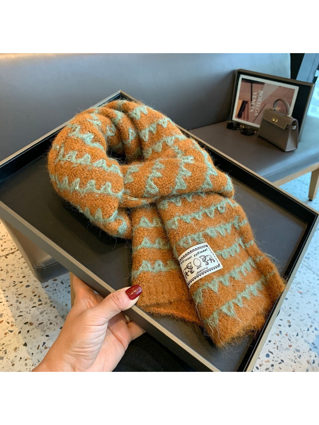 Orange knit scarf looped on a tray, with contrasting zigzag bands and an elephant patch