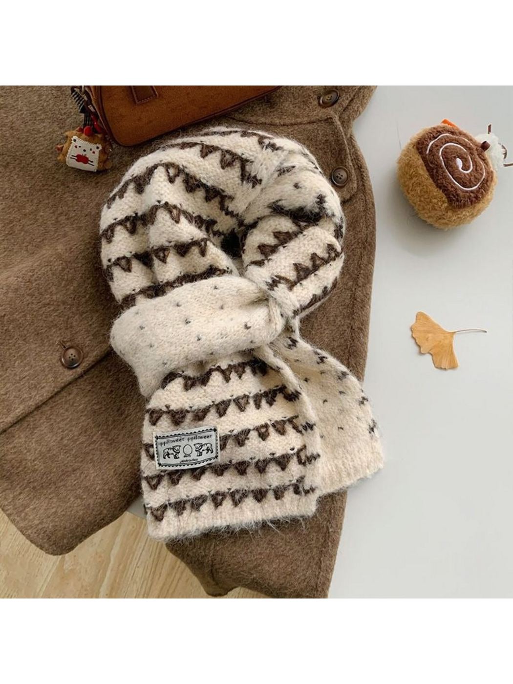 Ivory knit scarf with dark triangular bands and an elephant patch, looped over a coat