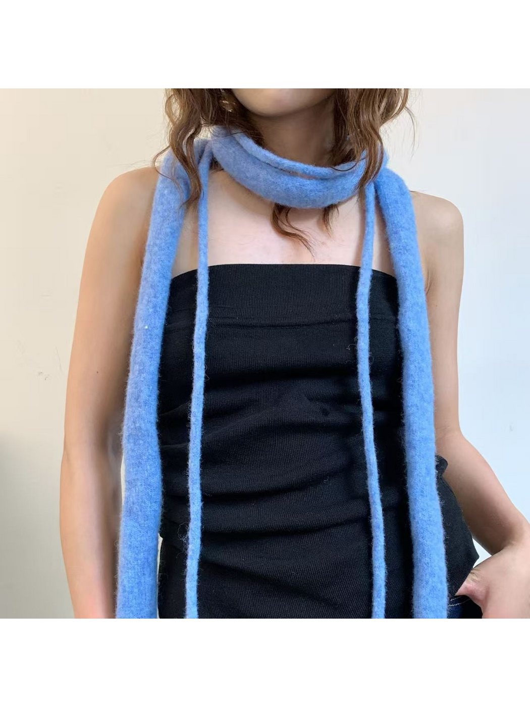 Blue narrow scarf worn loosely around the neck over a black top