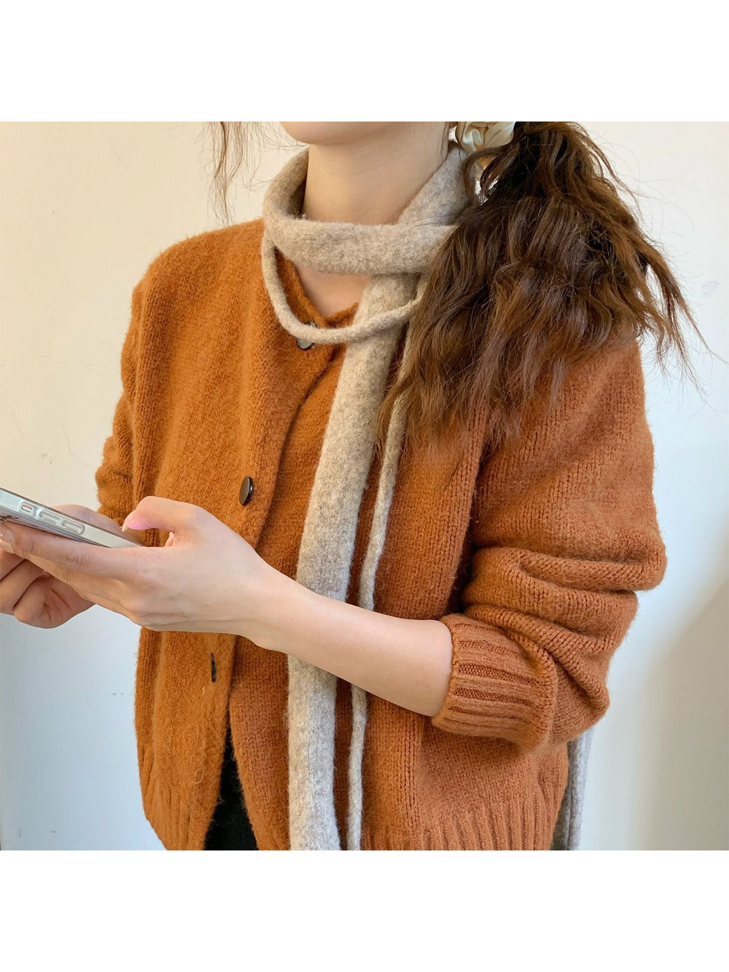 Beige narrow scarf worn around the neck over an orange cardigan