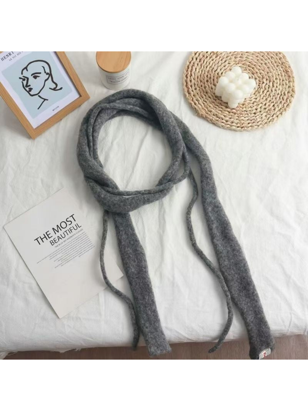 Gray fuzzy narrow scarf arranged in a loose loop on white fabric