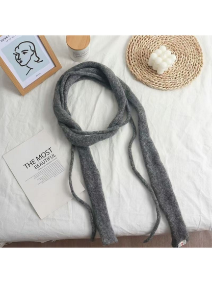 Gray fuzzy narrow scarf arranged in a loose loop on white fabric