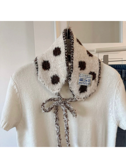 Beige polka-dot hood-shaped scarf with contrasting trim displayed over a white sweater